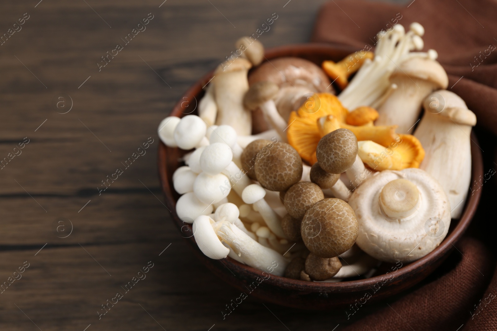 Different raw mushrooms in bowl on wooden table, closeup. Space for text Photo of Different raw mushrooms in bowl on wooden table, closeup. Space for text