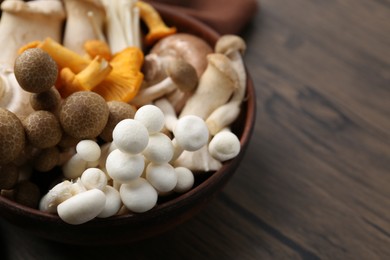 Photo of Different raw mushrooms in bowl on wooden table, closeup. Space for text