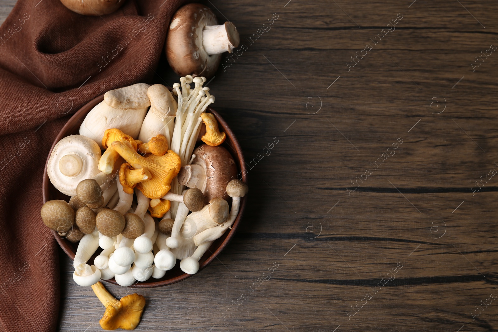 Different raw mushrooms in bowl on wooden table, flat lay. Space for text Photo of Different raw mushrooms in bowl on wooden table, flat lay. Space for text