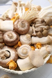Photo of Different raw mushrooms in wicker basket on white tiled table, closeup