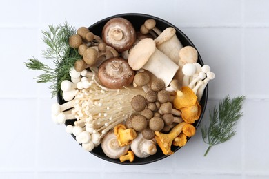 Photo of Different raw mushrooms in bowl and dill on white tiled table, flat lay