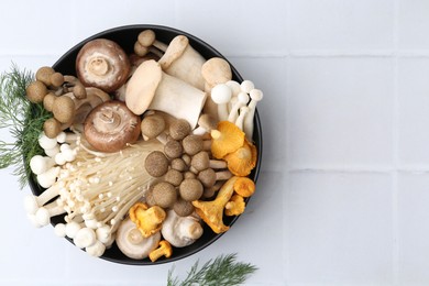 Photo of Different raw mushrooms in bowl and dill on white tiled table, flat lay. Space for text