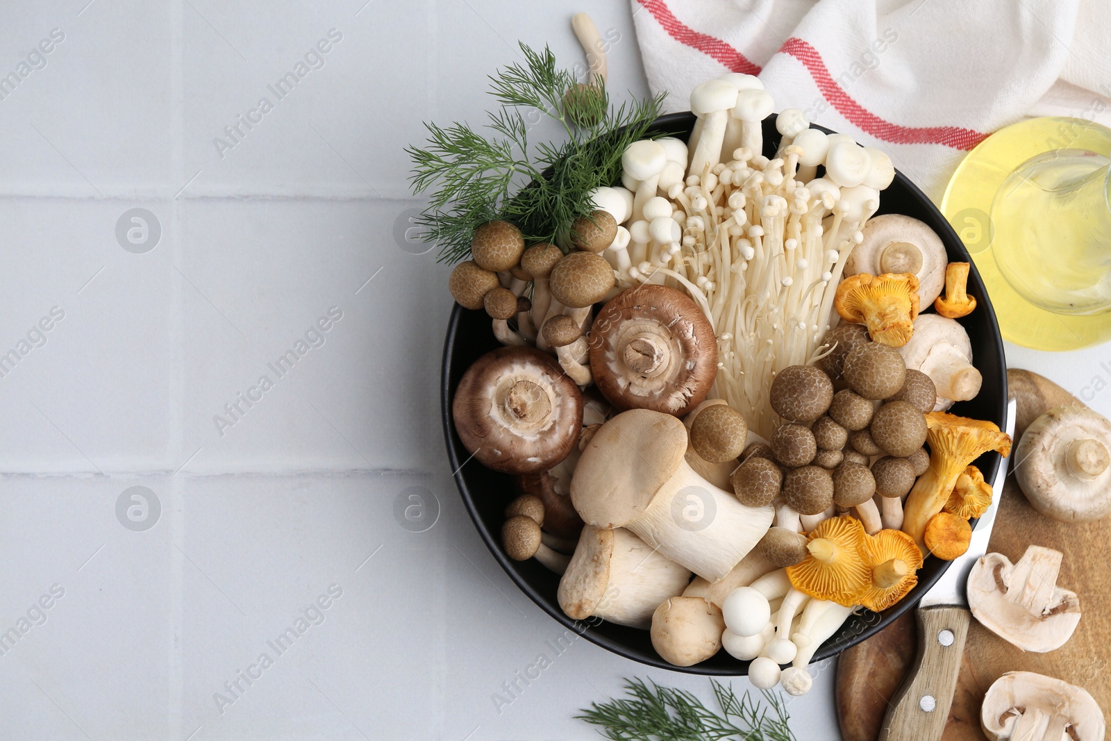 Photo of Different raw mushrooms in bowl and dill on white tiled table, flat lay. Space for text