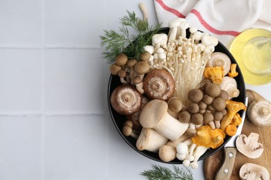 Photo of Different raw mushrooms in bowl and dill on white tiled table, flat lay. Space for text