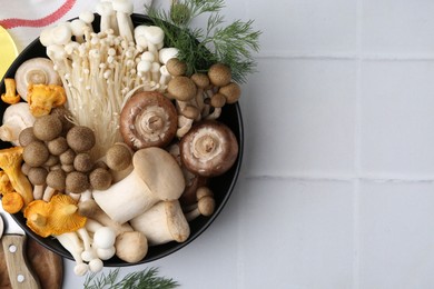 Photo of Different raw mushrooms in bowl and dill on white tiled table, flat lay. Space for text
