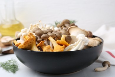 Photo of Different raw mushrooms in bowl on white tiled table, closeup