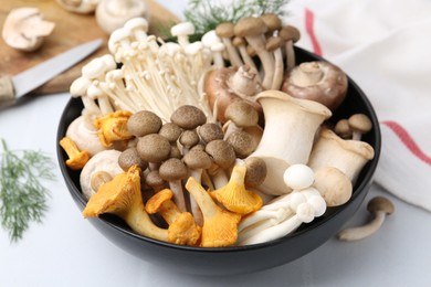 Photo of Different raw mushrooms in bowl on white tiled table, closeup