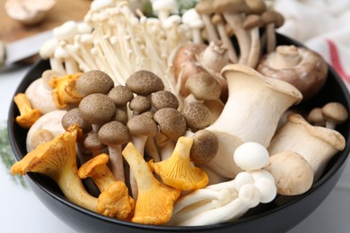 Photo of Different raw mushrooms in bowl on white table, closeup