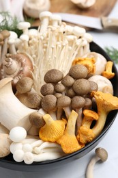 Photo of Different raw mushrooms in bowl on white table, closeup