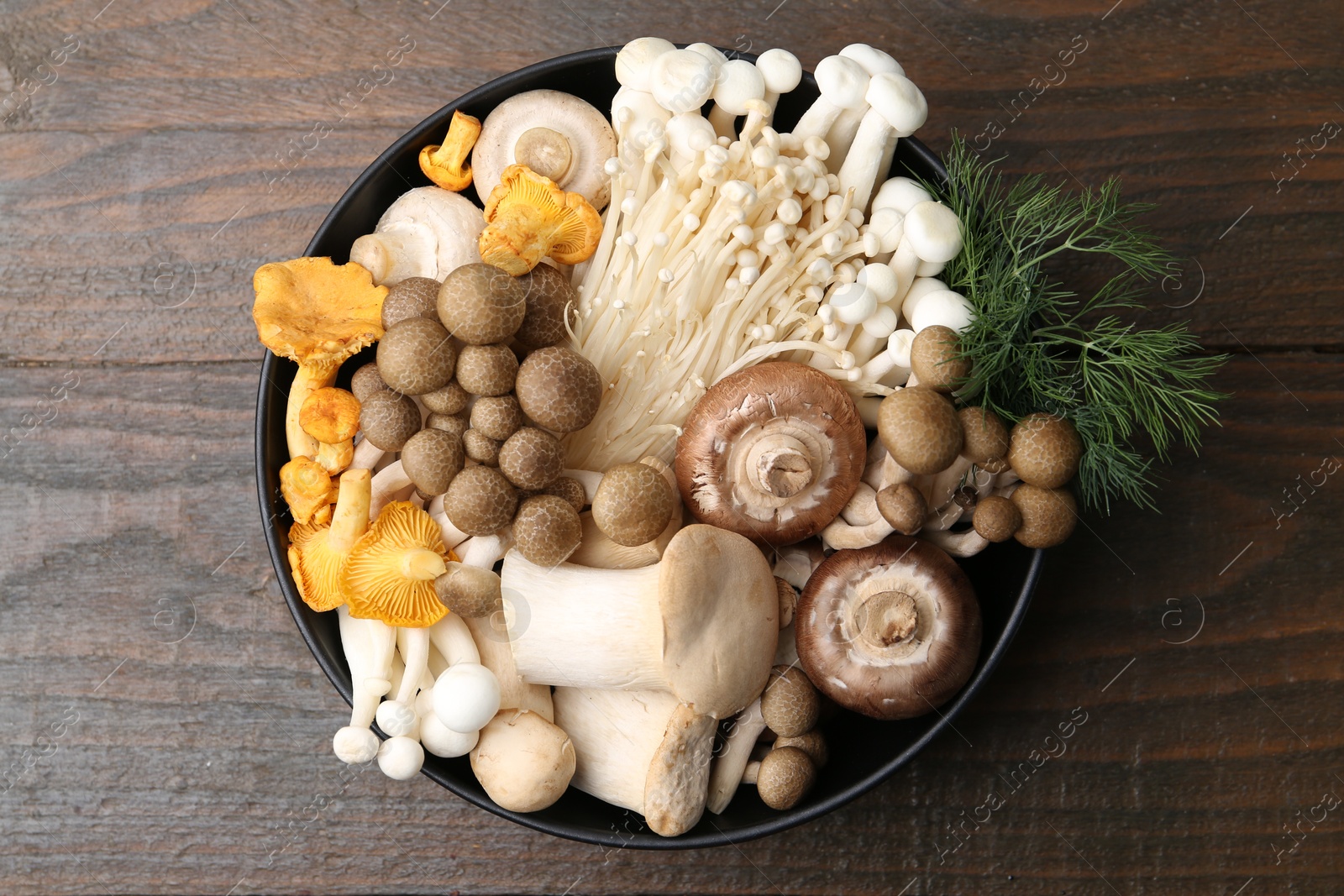 Different raw mushrooms and dill in bowl on wooden table, top view Photo of Different raw mushrooms and dill in bowl on wooden table, top view
