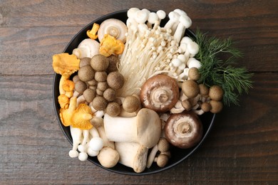 Photo of Different raw mushrooms and dill in bowl on wooden table, top view