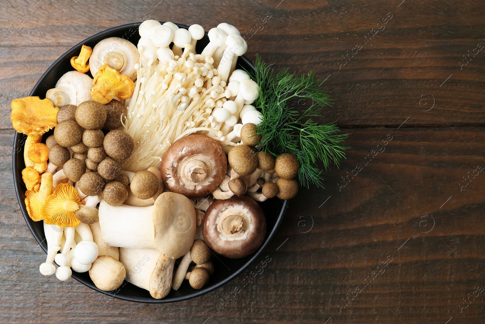 Different raw mushrooms and dill in bowl on wooden table, top view. Space for text Photo of Different raw mushrooms and dill in bowl on wooden table, top view. Space for text