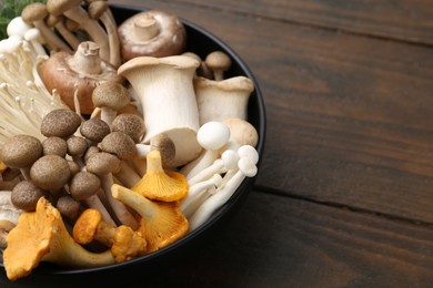 Photo of Different raw mushrooms in bowl on wooden table, closeup. Space for text