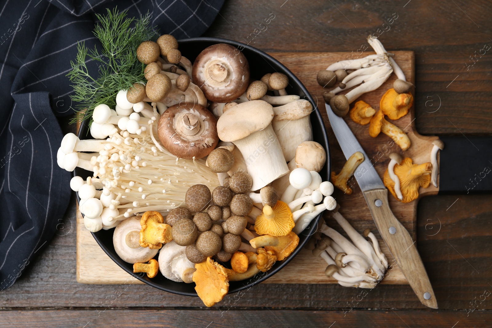 Photo of Different raw mushrooms in bowl and knife on wooden table, flat lay