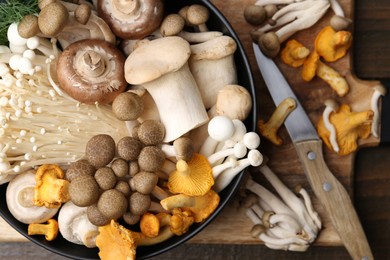 Photo of Different raw mushrooms in bowl and knife on wooden table, top view