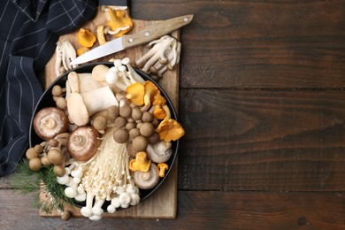 Photo of Different raw mushrooms in bowl and knife on wooden table, top view. Space for text