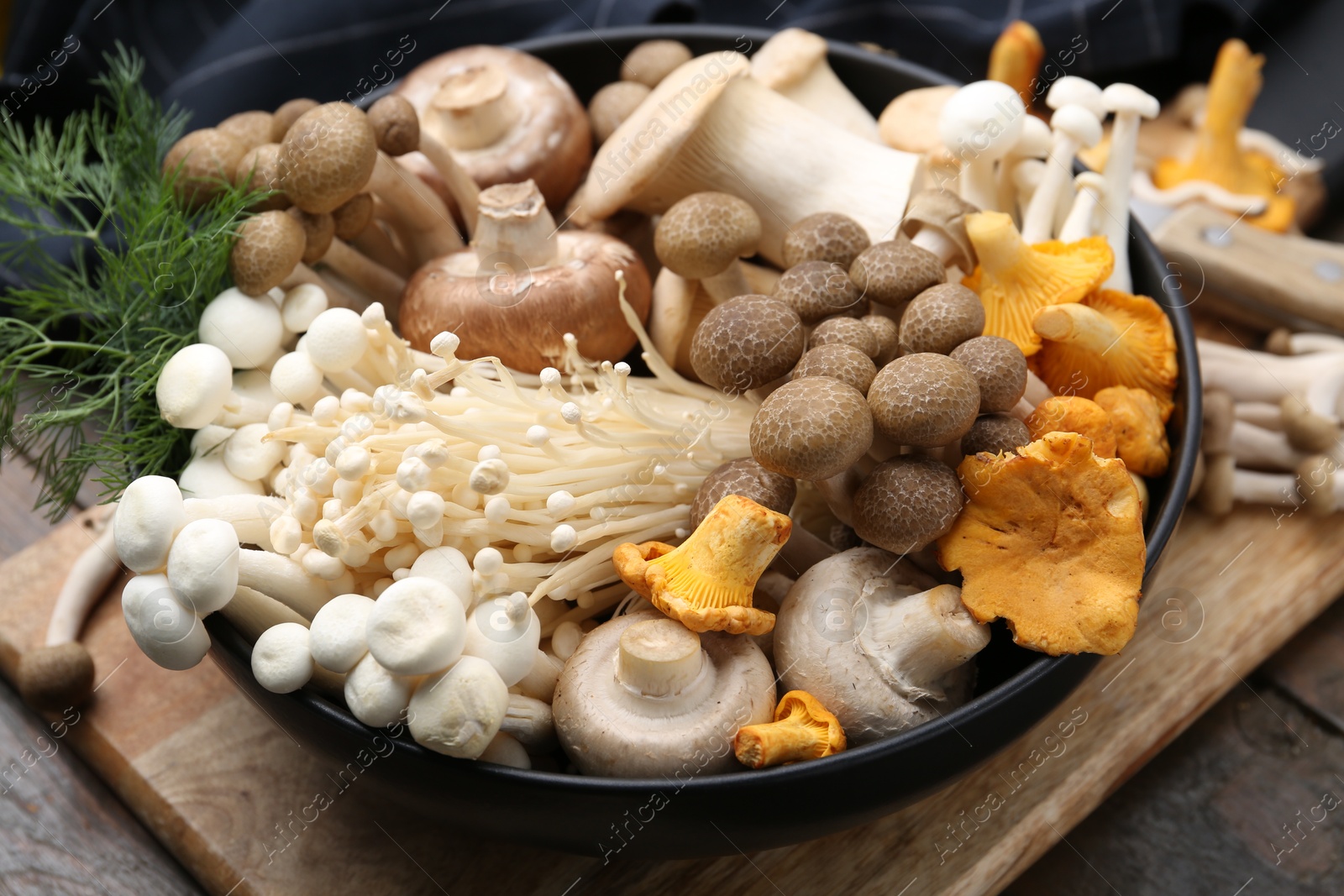 Photo of Different raw mushrooms and dill in bowl on wooden table, closeup