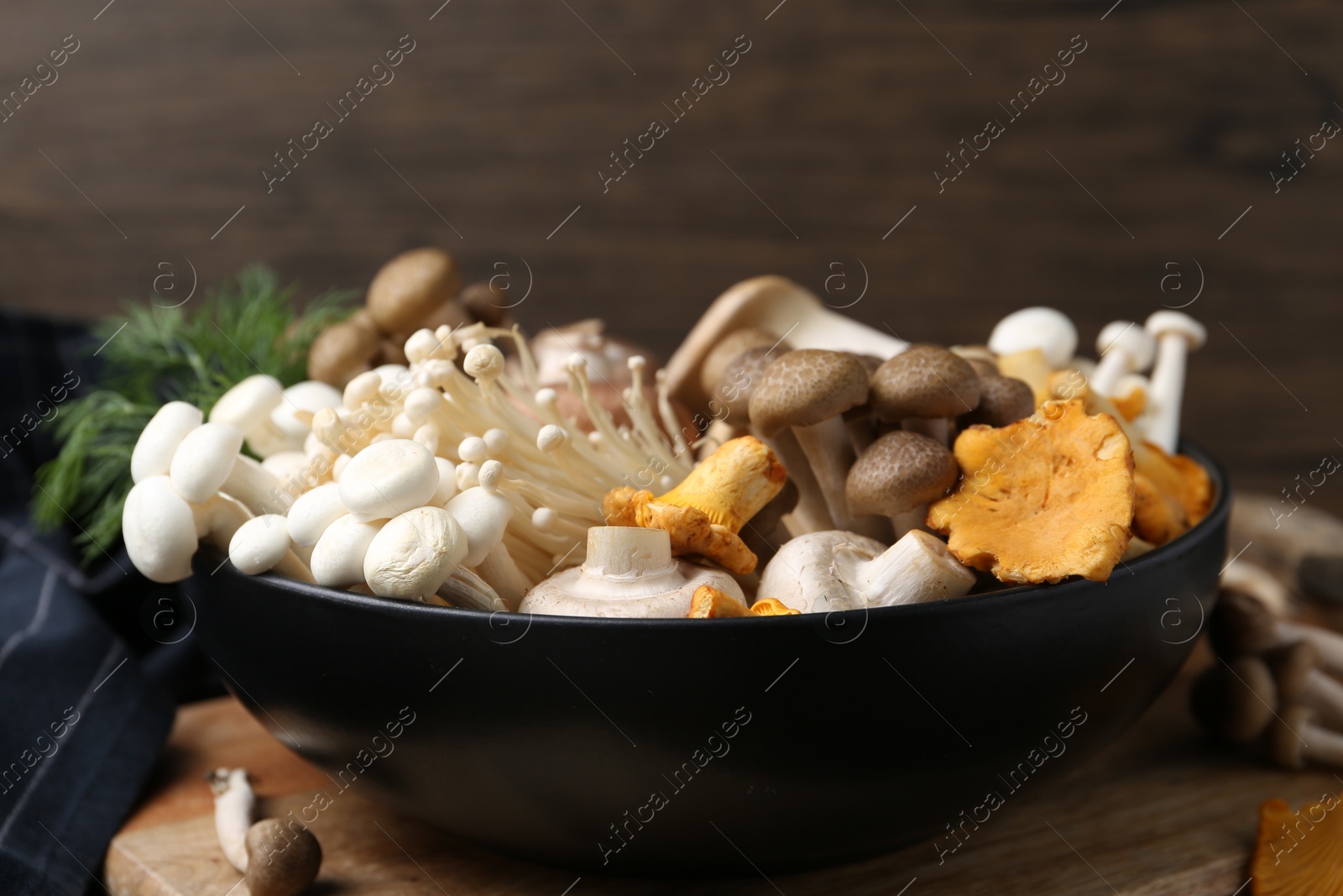 Photo of Different raw mushrooms in bowl on table against wooden background, closeup