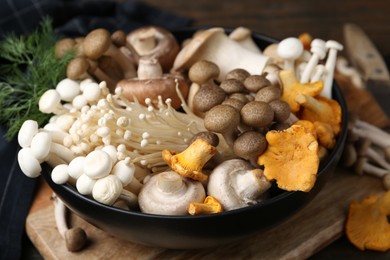 Photo of Different raw mushrooms in bowl on table against wooden background, closeup