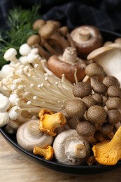 Photo of Different raw mushrooms in bowl on wooden table, closeup