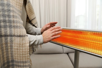 Image of Man with plaid warming his hands near electric heater at home, closeup