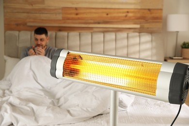 Image of Man in room with electric heater, selective focus