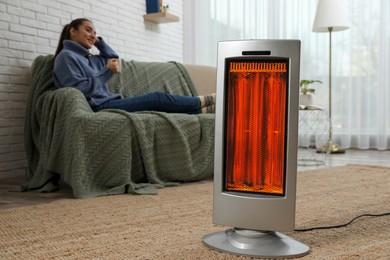 Image of Woman on sofa in room with electric heater, selective focus