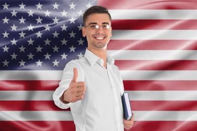 Image of Teacher with book showing thumbs-up against flag of USA. Language school