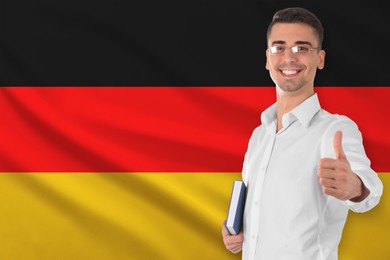 Image of Teacher with book showing thumbs-up against flag of Germany. Language school