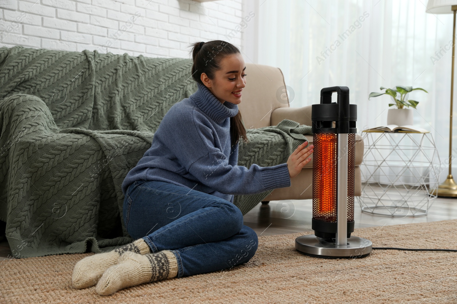 Woman warming her hand near electric heater on floor at home Image of Woman warming her hand near electric heater on floor at home