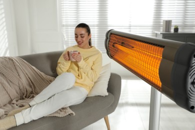 Image of Woman on sofa in room with electric heater, selective focus