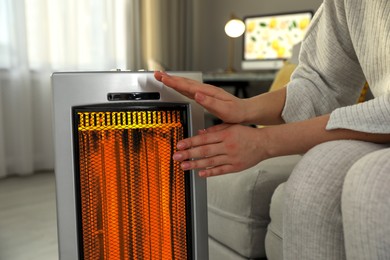 Image of Woman warming her hands near electric heater at home, closeup