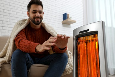 Image of Man warming his hands near electric heater at home