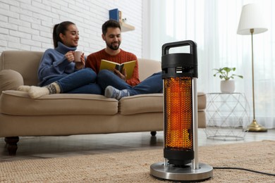 Image of Couple on sofa in room with electric heater, selective focus
