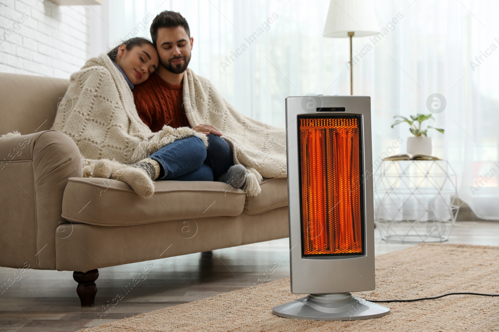 Couple on sofa in room with electric heater Image of Couple on sofa in room with electric heater