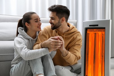 Image of Couple warming their hands near electric heater at home