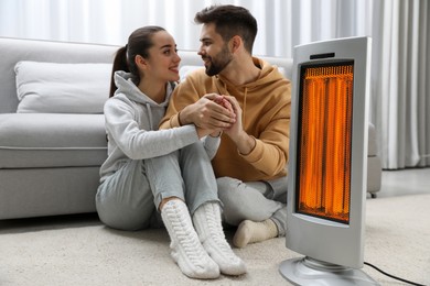 Image of Couple warming their hands near electric heater on floor at home