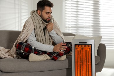 Image of Man warming his hand near electric hand on sofa at home