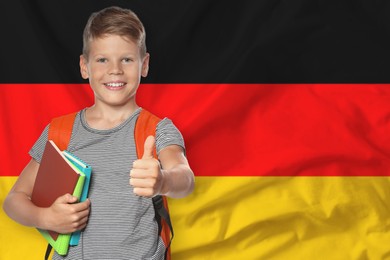 Image of Little boy with backpack and notebooks showing thumbs-up against flag of Germany. Language school