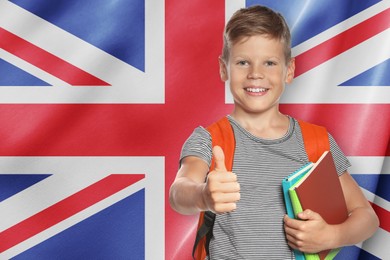 Image of Little boy with backpack and notebooks showing thumbs-up against flag of United Kingdom. Language school