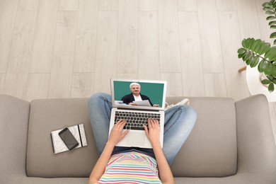 Image of E-learning concept. Student having online video chat with teacher via laptop on sofa at home, top view