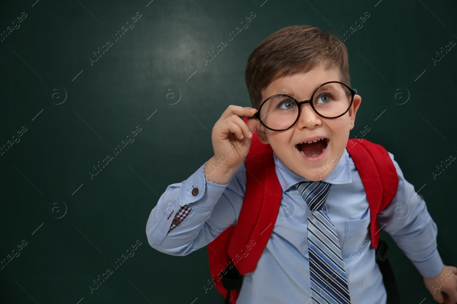 Funny little child wearing glasses near chalkboard, space for text. First time at school Photo of Funny little child wearing glasses near chalkboard, space for text. First time at school