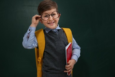 Photo of Cute little child wearing glasses near chalkboard. First time at school