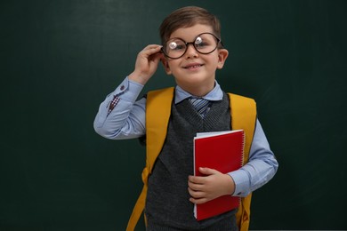 Photo of Cute little child wearing glasses near chalkboard. First time at school