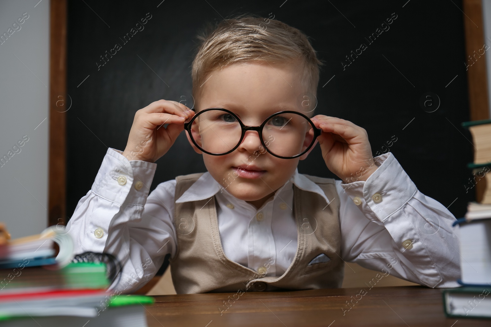 Cute little child wearing glasses at desk in classroom. First time at school Photo of Cute little child wearing glasses at desk in classroom. First time at school