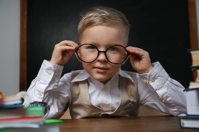 Photo of Cute little child wearing glasses at desk in classroom. First time at school