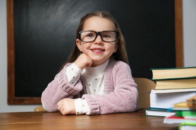 Photo of Cute little child wearing glasses at desk in classroom. First time at school