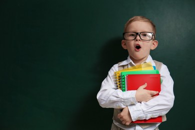 Photo of Cute little child wearing glasses near chalkboard, space for text. First time at school