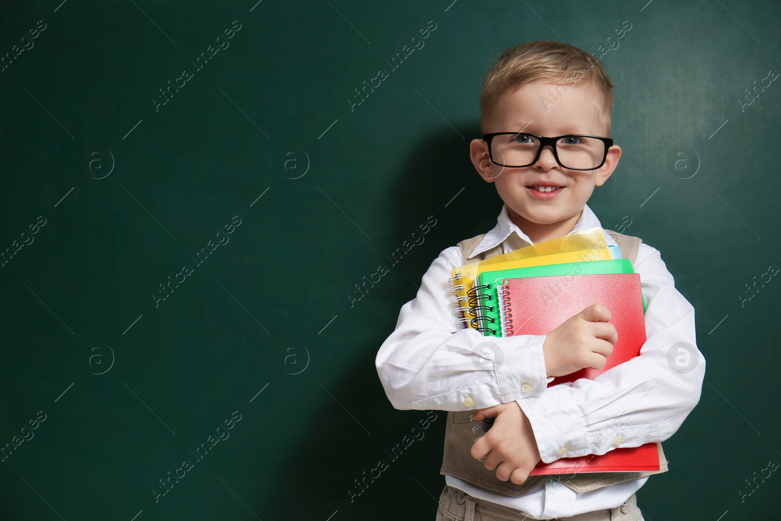Cute little child wearing glasses near chalkboard, space for text. First time at school Photo of Cute little child wearing glasses near chalkboard, space for text. First time at school