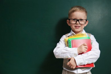 Photo of Cute little child wearing glasses near chalkboard, space for text. First time at school